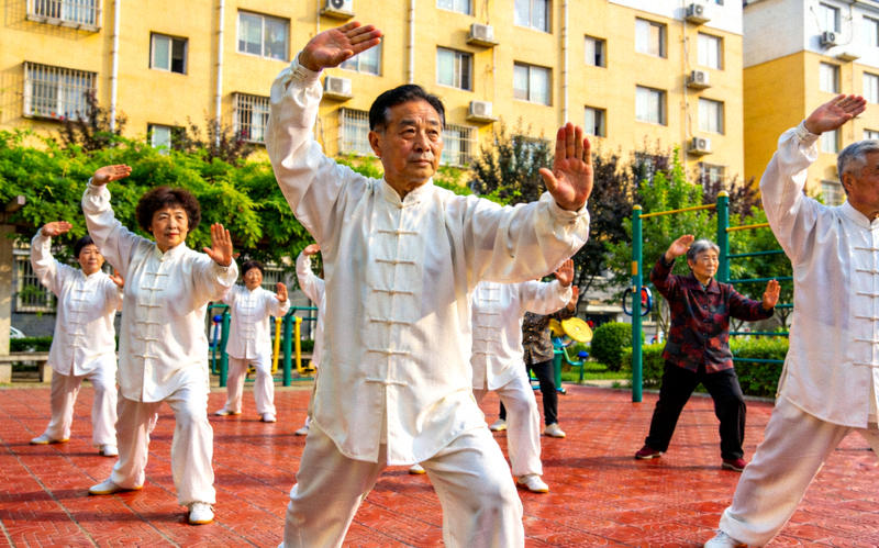 社区居民在小区广场上跟随社会体育指导员一起练习太极拳的和谐场景