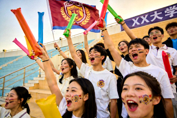 热情的大学生球迷在看台上挥舞校旗和助威棒，脸上涂着校徽油彩，为球队呐喊